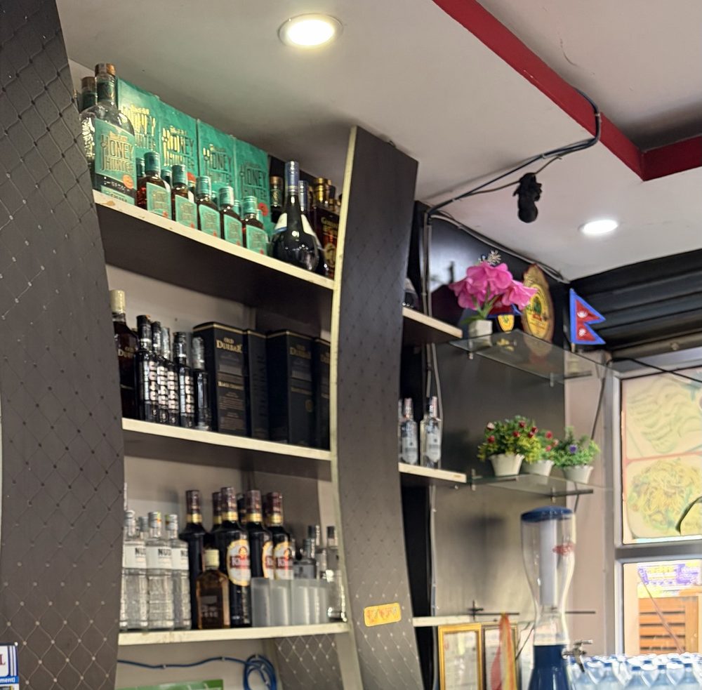 The counter at Api Hotel, with shelves of bottles, flowers and a small Nepali flag by the window